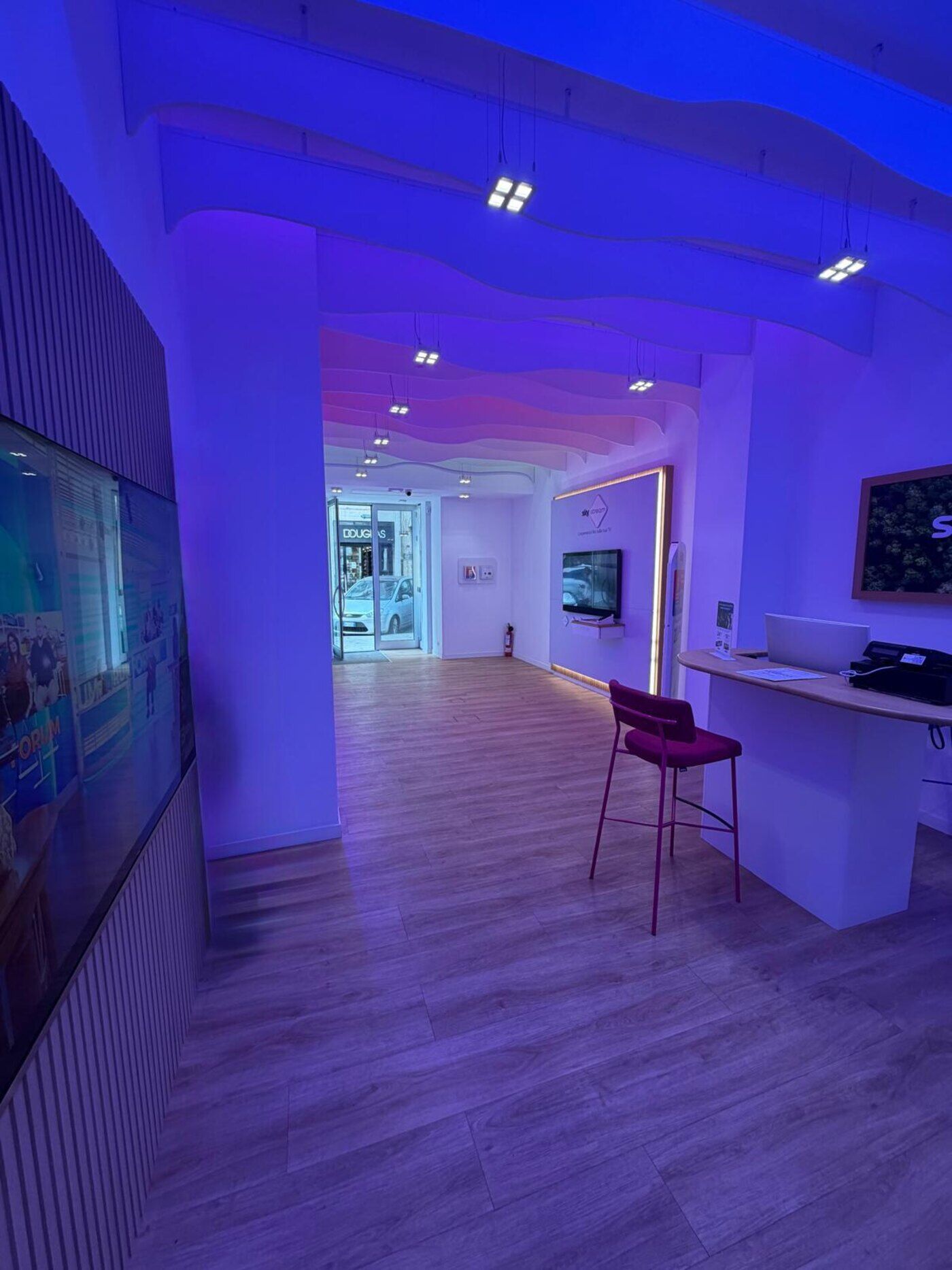 Bancone reception nello store 3sat di Taranto, sgabelli rossi, illuminazione viola.